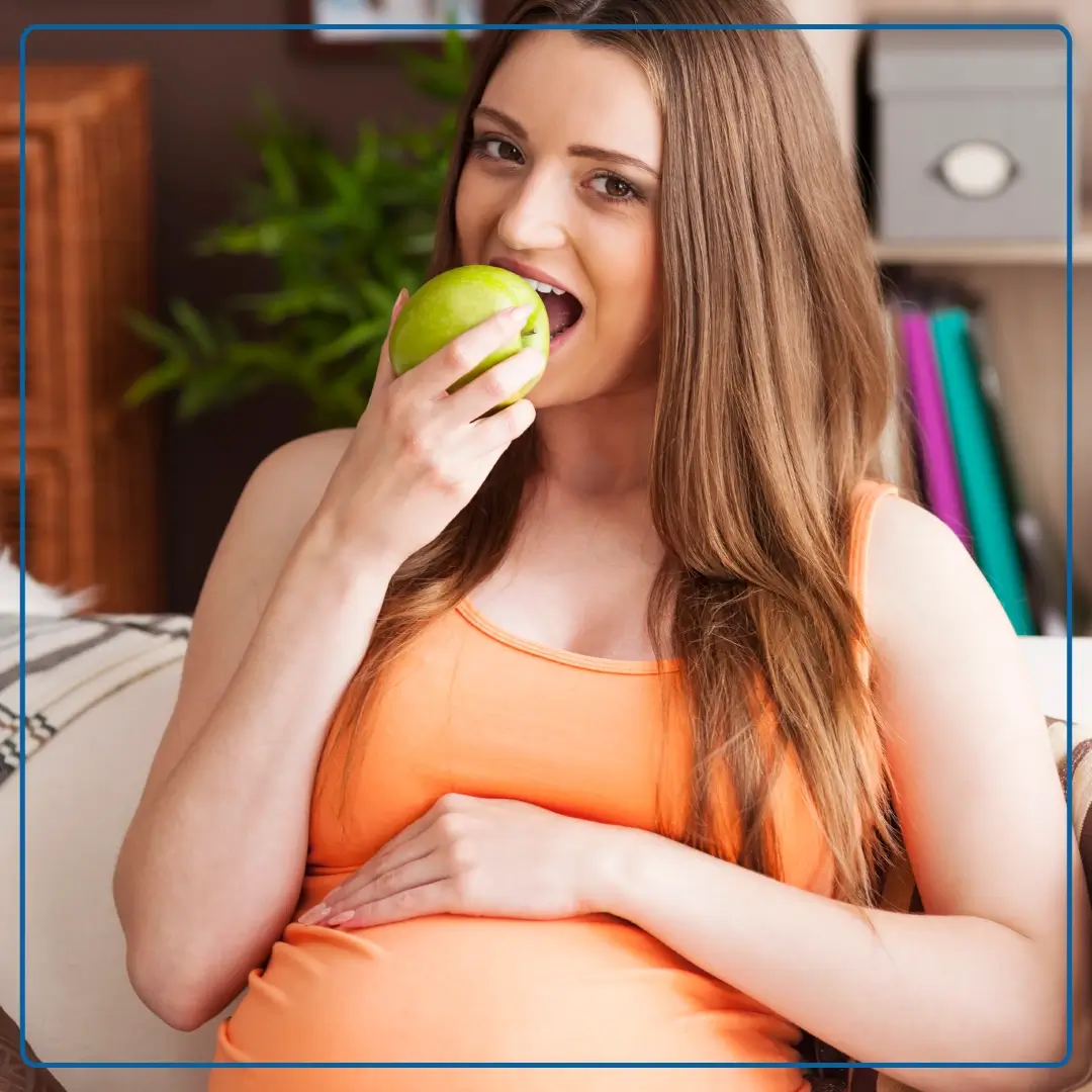 Immagine di una donna incinta che mangia una mela. Foto di accompagnamento all'articolo dedicato a "Alimentazione e fertilità".