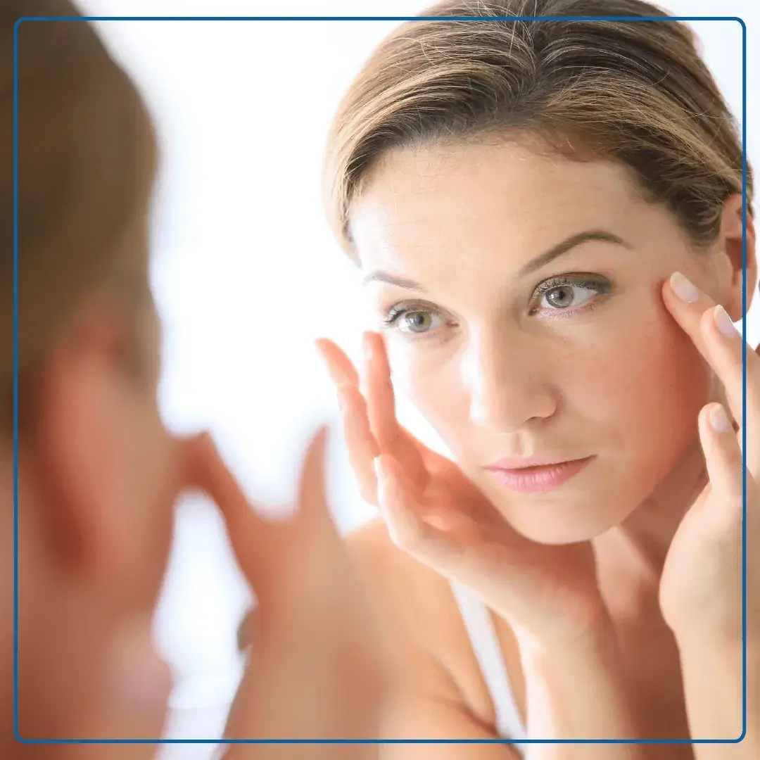 Immagine di una donna che si guarda alla specchio e si tocca con le dita il viso. Foto utilizzata per la pagina Visita di medicina estetica.